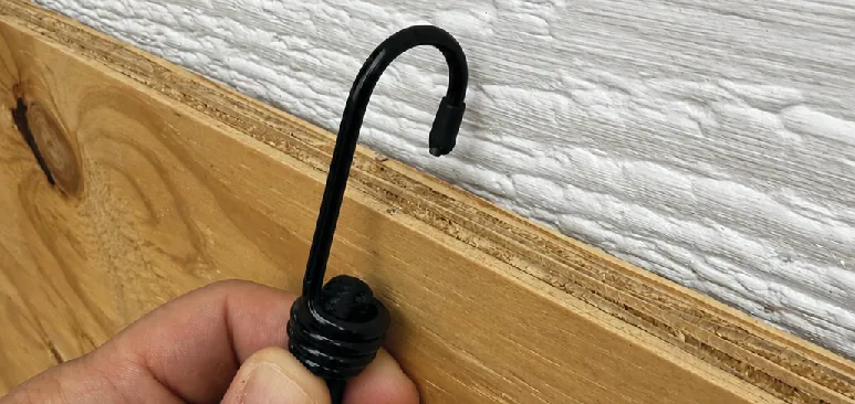 Hand hooking the black bungee over the top edge of a plywood panel
